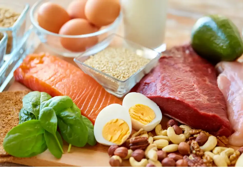 High protein meal prep ingredients including salmon, beef, eggs, nuts, spinach, and grains arranged on a wooden surface.